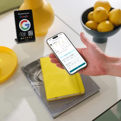 Hand holding smartphone showing Google review interface near table display for tap NFC and QR code reviews