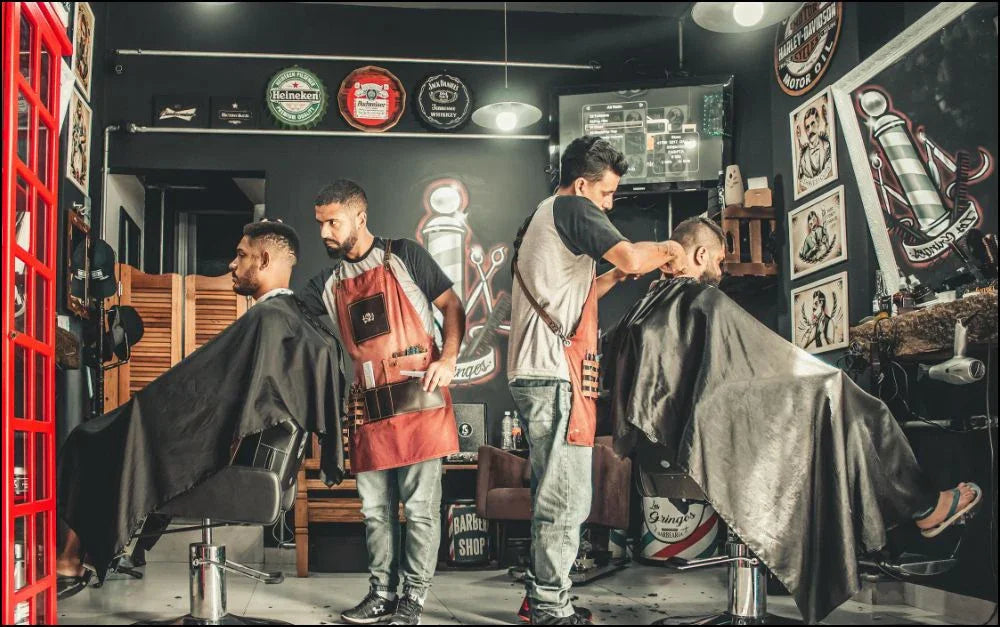 Two barbers cutting hair of two clients in a vintage-style barbershop with black walls and retro decor