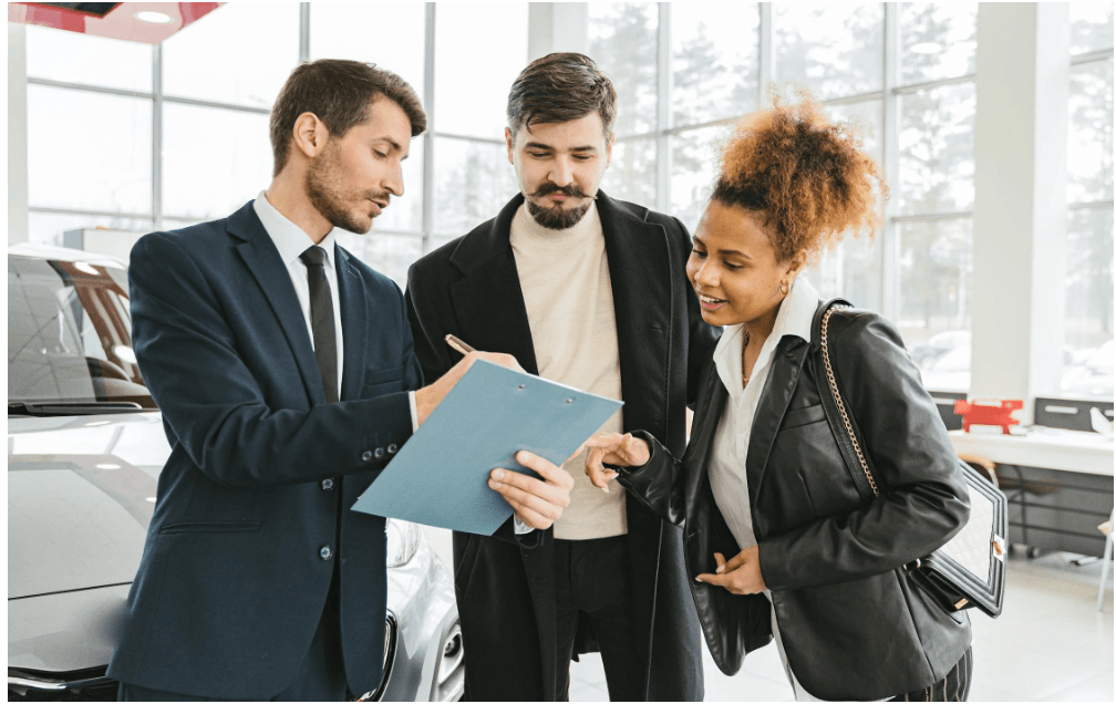 Sales professional in suit discussing documents with couple in modern car showroom