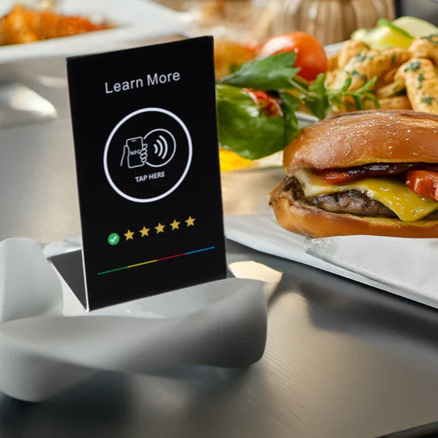 Table tent card with NFC Tap Here for Google reviews next to cheeseburger and salad on table