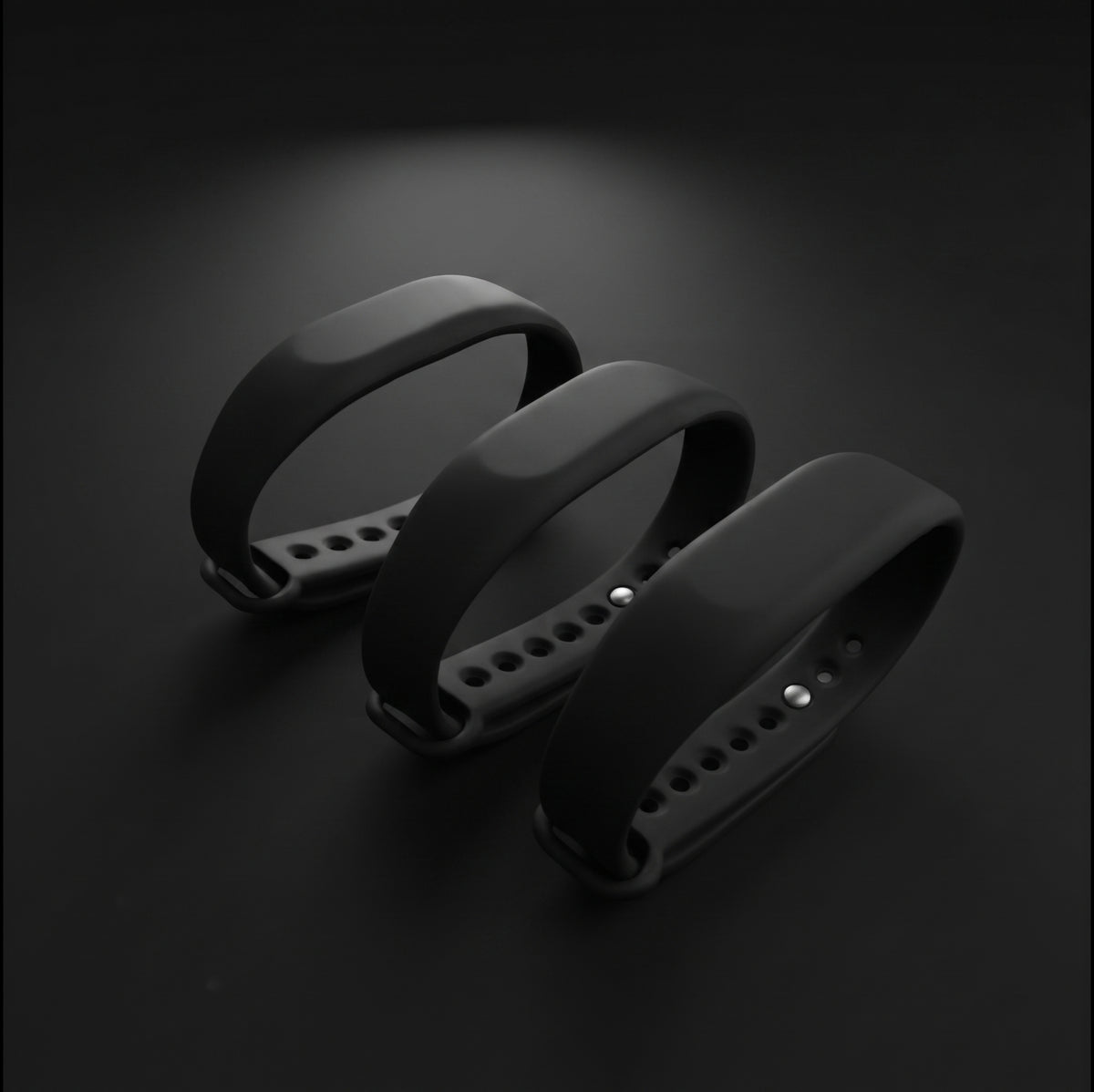 Three black silicone smartwatch bands arranged diagonally on a dark, reflective surface.